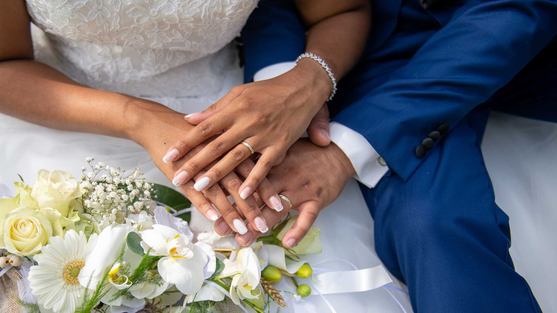 Mains unies des mariés avec alliances et bouquet.