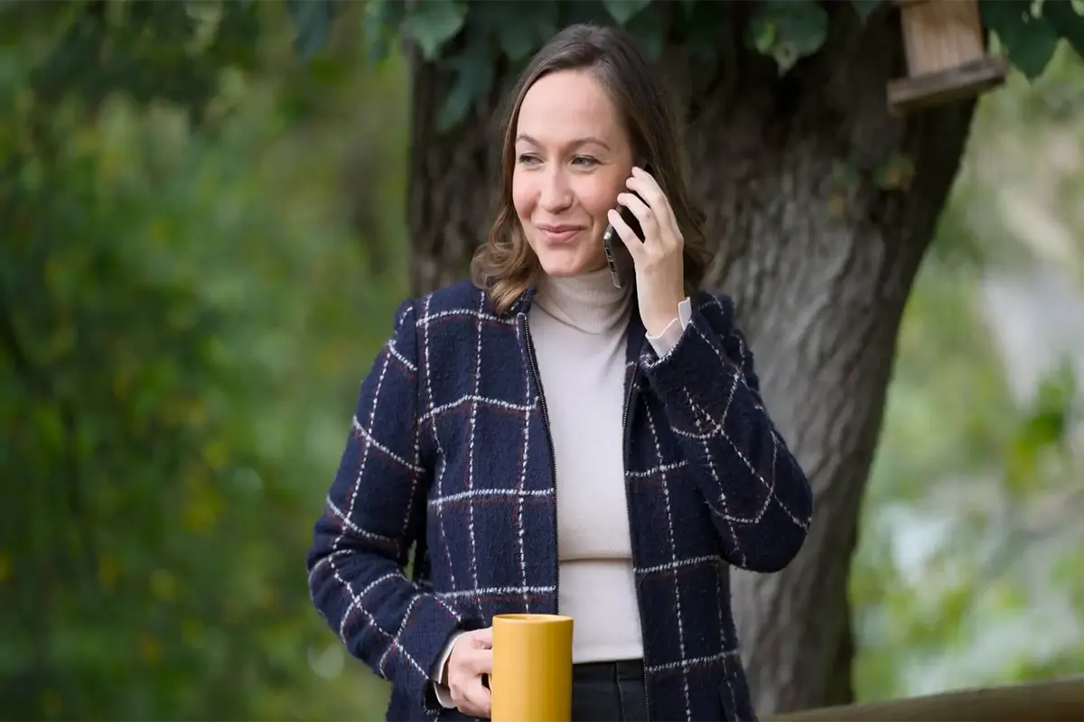 Femme souriante avec téléphone et tasse jaune.