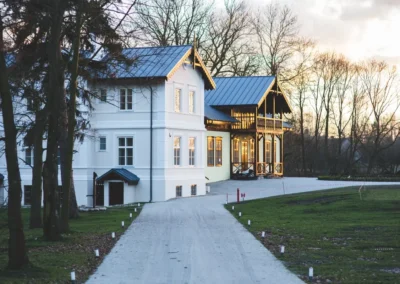 Maison blanche entourée d'arbres, chemin au coucher du soleil.
